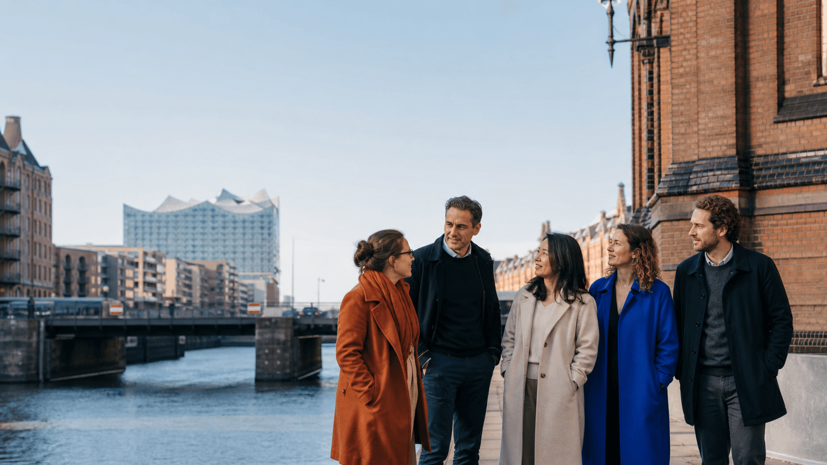 A diverse Dudoxx team walking beside Hamburg’s Speicherstadt with the Elbphilharmonie beyond
